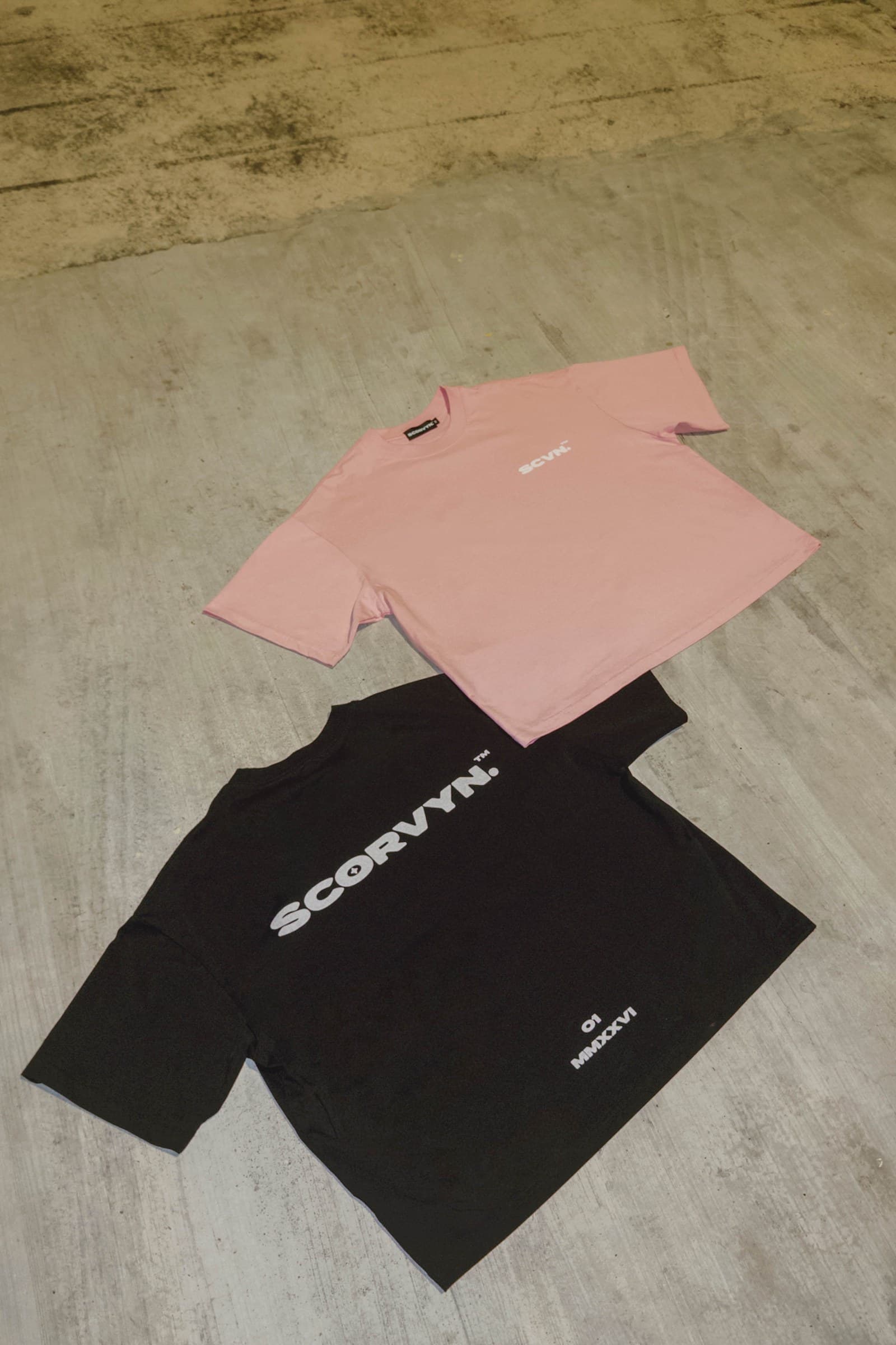 Both tees laid out on concrete, powder front and ink back print