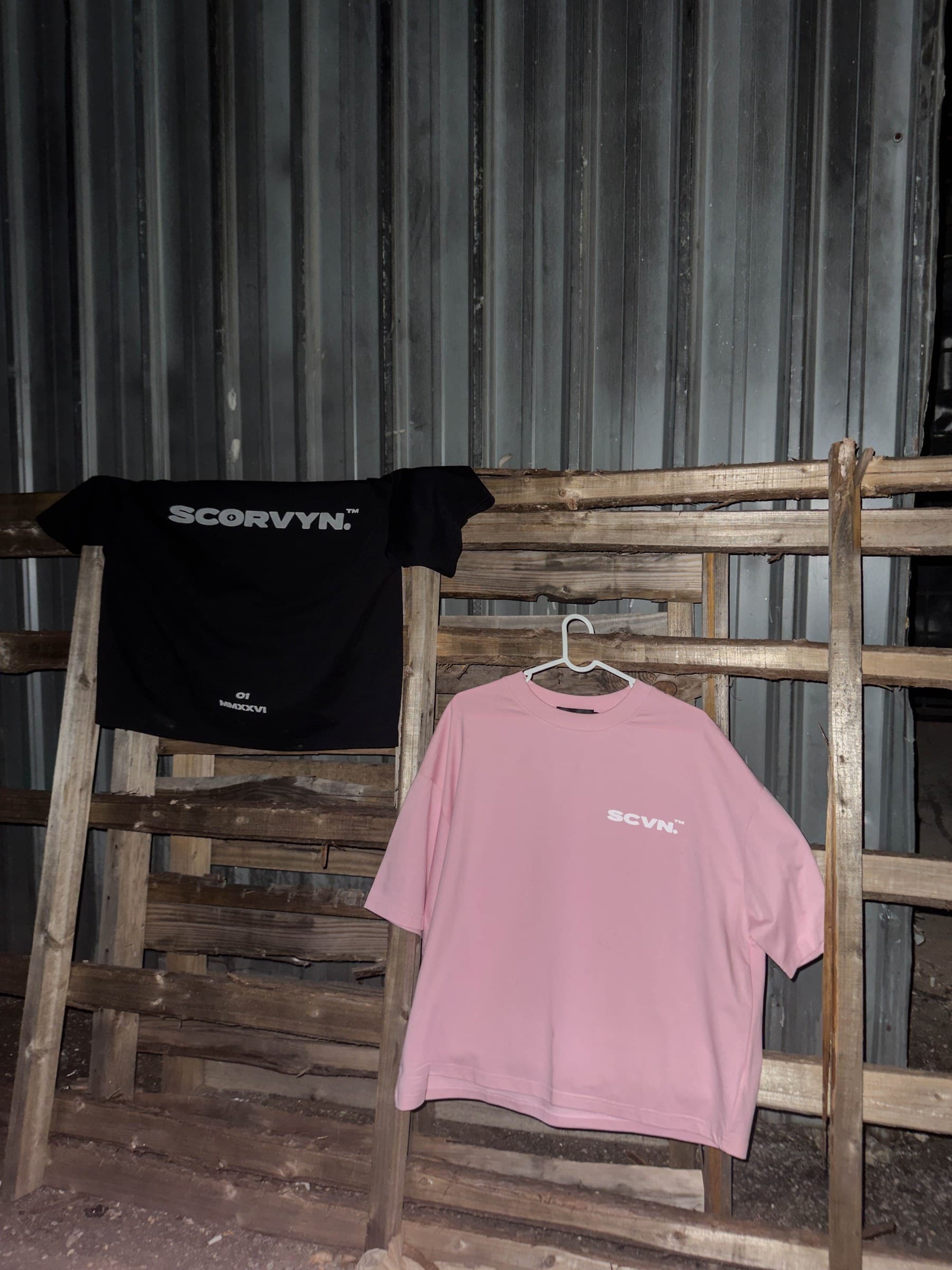 Both colourways on a timber rack at night, ink draped over the rail and powder on a hanger