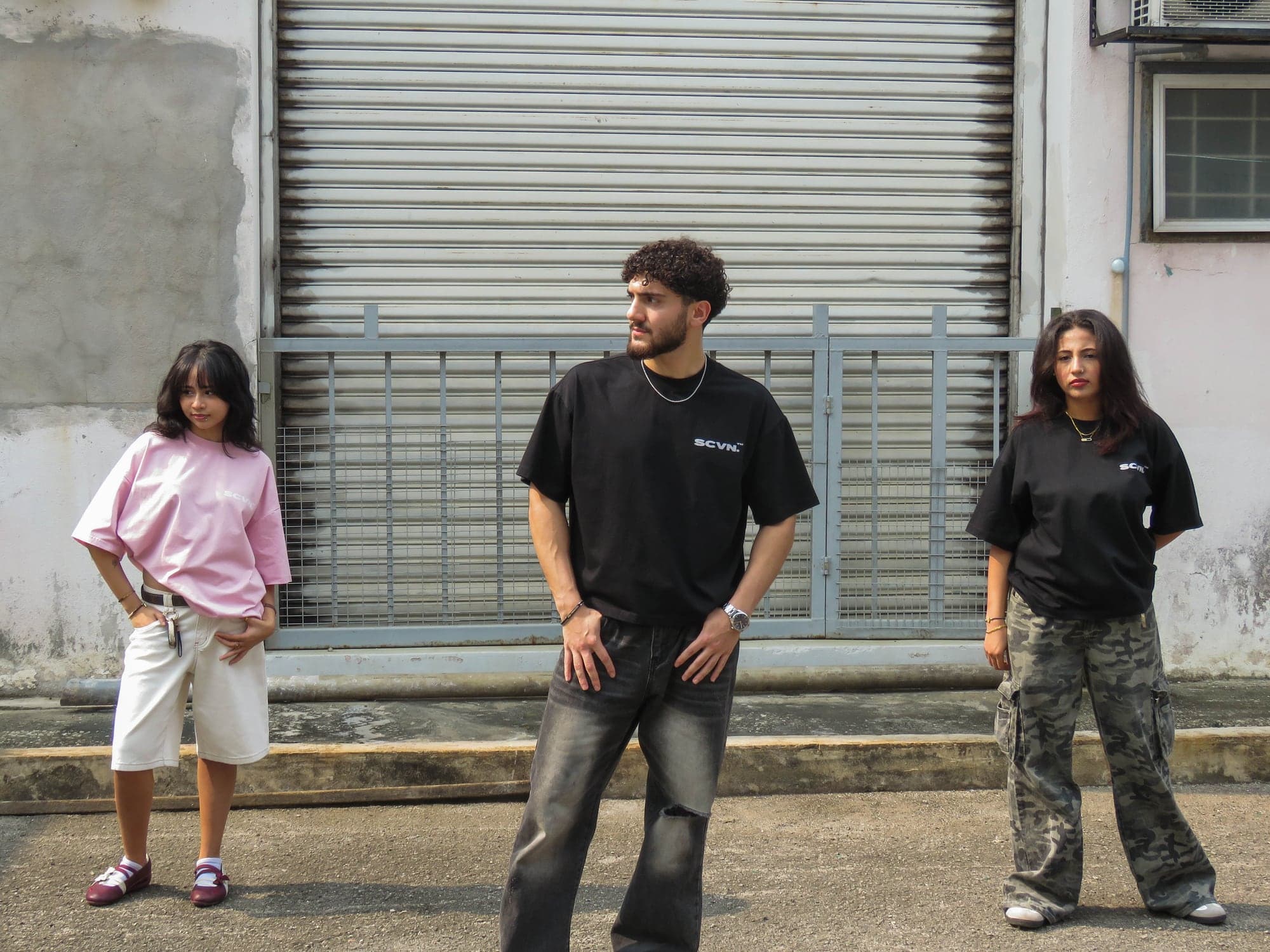 Three models in SCVN.01, ink and powder, standing far apart in a street